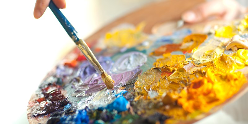artist brush mix color oil painting on palette is holding in his hand closeup
